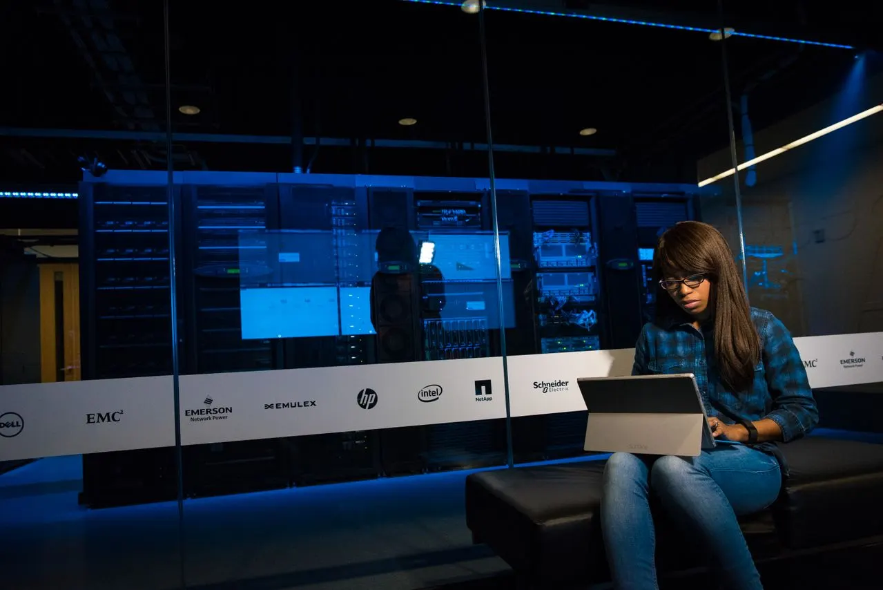 A woman working on a tablet in front of a server room